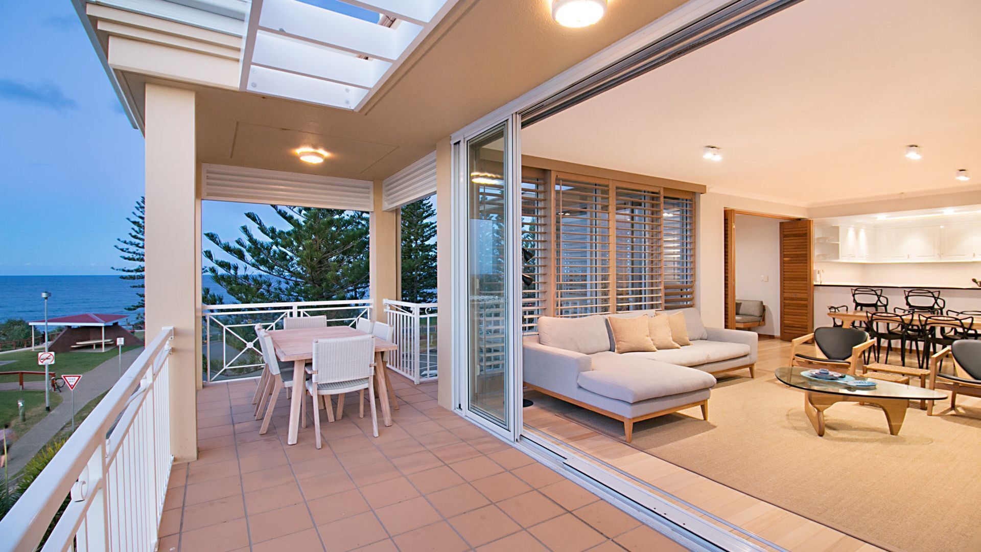 Un balcon spacieux offrant une vue sur l’océan, un coin salon avec un canapé et des fauteuils, et un espace repas avec une table et des chaises.