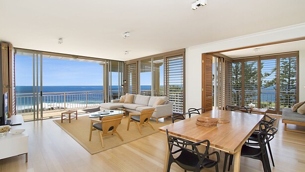 A spacious living area with a large wooden table and multiple chairs, a sofa, and a balcony with a view of the ocean. - Orion Unit 7 Modern apartment with Wi-Fi included, overlooking Snapper Rocks and Rainbow Bay (Coolangatta)