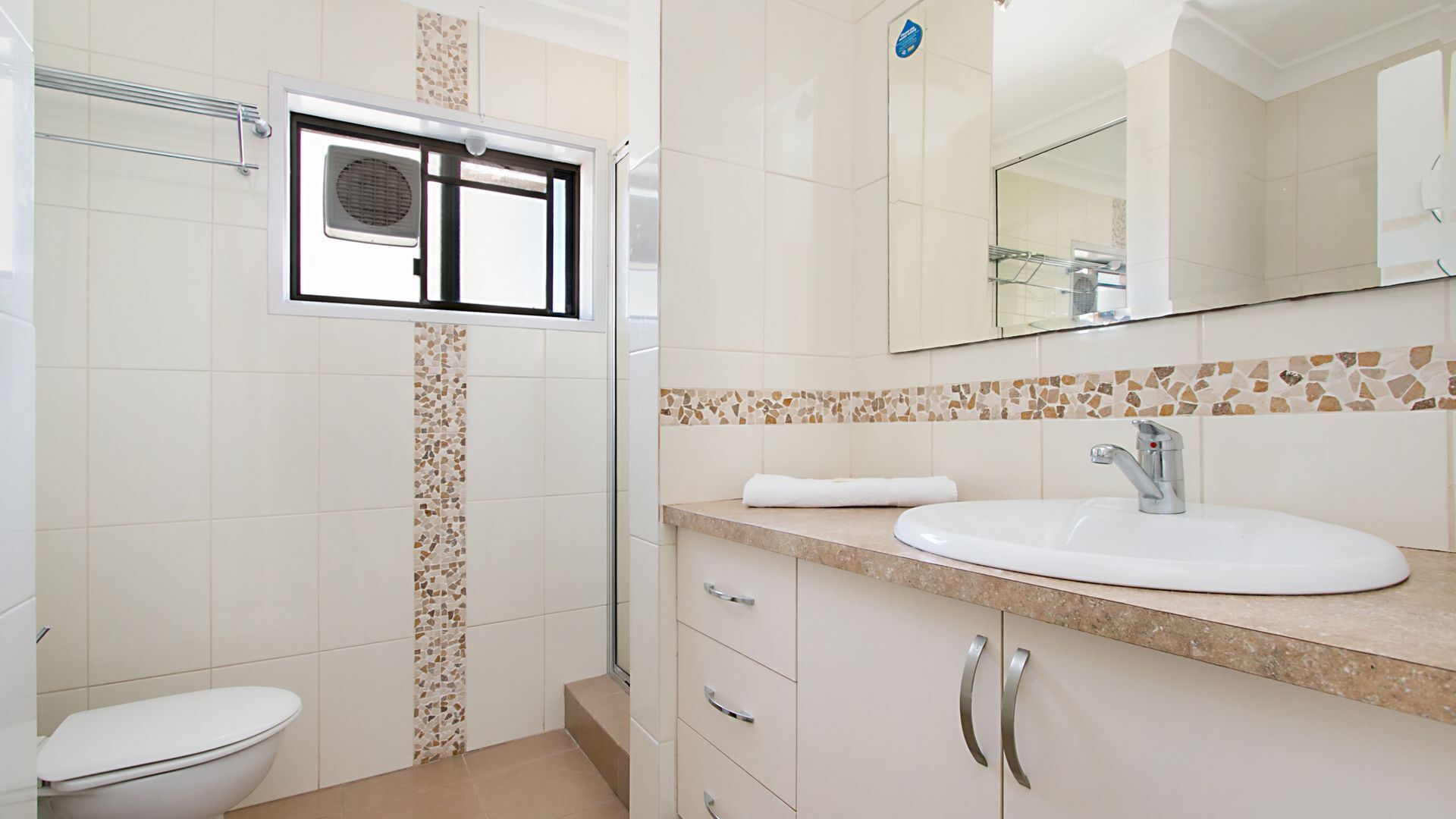 A bathroom with a toilet, a shower with a glass door, a sink with a mirror, and tiled walls.