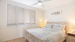 A bedroom with a bed, two bedside tables, a ceiling fan, and a window with blinds. - Kirra Vista Apartments Unit 18 Kirra Beachfront, easy walk to shops, cafes and clubs with Wi-Fi (Coolangatta)