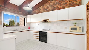 Cocina moderna con armarios blancos, horno negro, microondas y ventana con vistas a árboles.