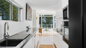 A modern kitchen with a stainless steel sink, a built-in oven, and a large window providing a view of trees. - Rainbow Pacific Unit 9- Stunning views over Rainbow Bay and Snapper Rocks. Swimming Pool. Wi-Fi (Coolangatta)