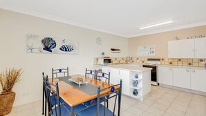 Una cocina moderna con armarios blancos, microondas y estufa. Cuenta con una zona de comedor con una mesa y sillas de madera.