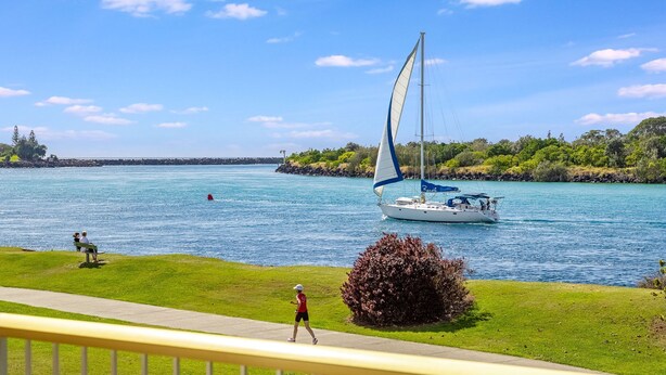 Un velero en un lago tranquilo, con una zona cubierta de hierba y un sendero en primer plano.