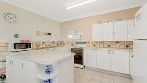 Una cocina con gabinetes blancos, un microondas, una estufa y un reloj en la pared.