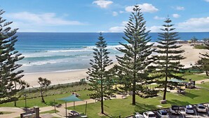 Vista de la playa con zona de estacionamiento y área verde con bancos.