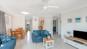 A modern living room with a blue sofa, wooden dining table, and a flat-screen TV on a wooden stand. - Cobden Court Unit 6 Walking distance to Rainbow Bay and Snapper Rocks beaches with Wi-Fi Inc. (Coolangatta)