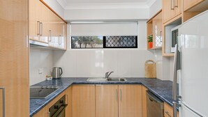 A compact kitchen with wooden cabinets, a stainless steel sink, and a built-in oven. - Cobden Court Unit 6 Walking distance to Rainbow Bay and Snapper Rocks beaches with Wi-Fi Inc. (Coolangatta)