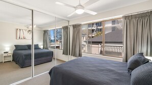 A modern hotel room with two beds, a large window with curtains, a ceiling fan, and a nightstand with a lamp. - Cobden Court Unit 6 Walking distance to Rainbow Bay and Snapper Rocks beaches with Wi-Fi Inc. (Coolangatta)