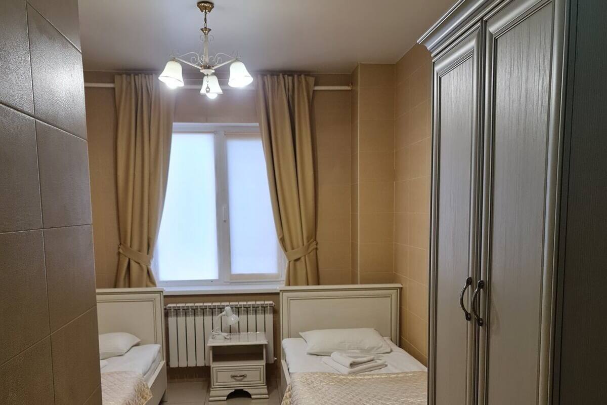 Une chambre avec deux lits, une armoire, un radiateur, une fenêtre avec des rideaux et un luminaire au plafond.