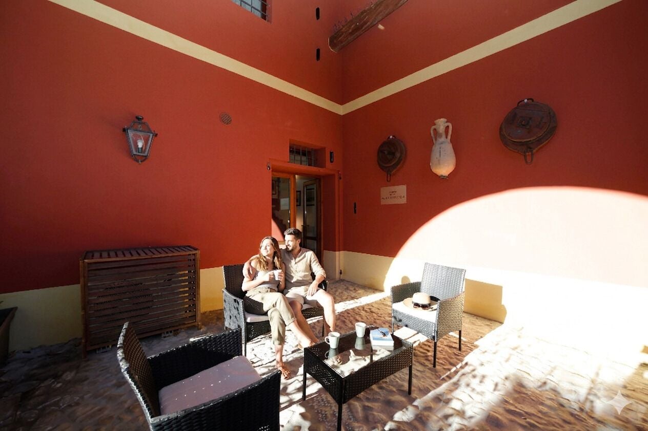 Une pièce avec un mur rouge, des meubles en osier, une petite table et une porte qui donne sur une autre pièce.