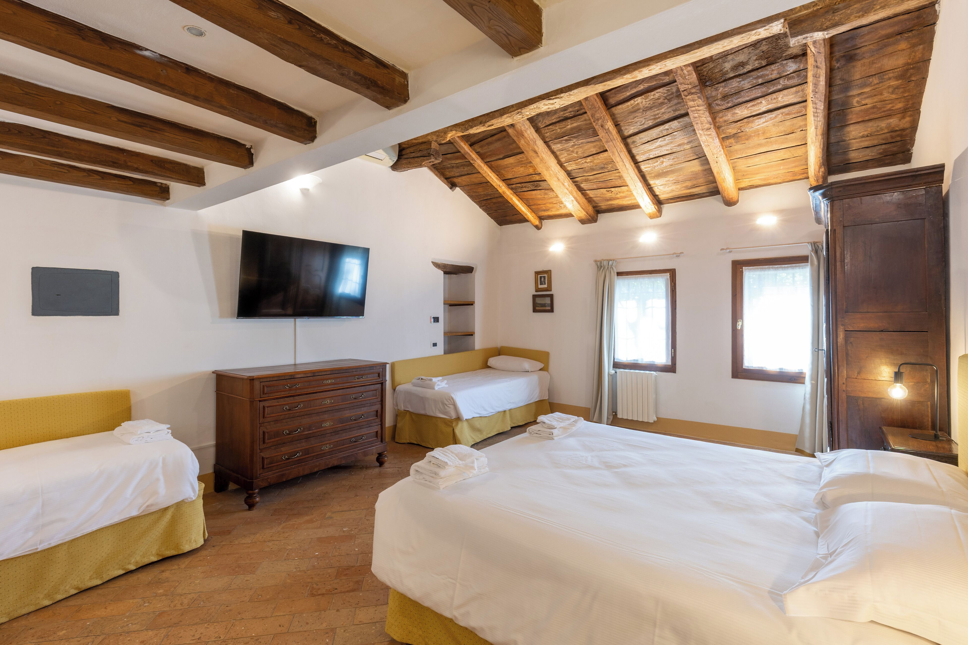 Un dormitorio con dos camas, vigas de madera en el techo, un televisor en la pared y un aparador.