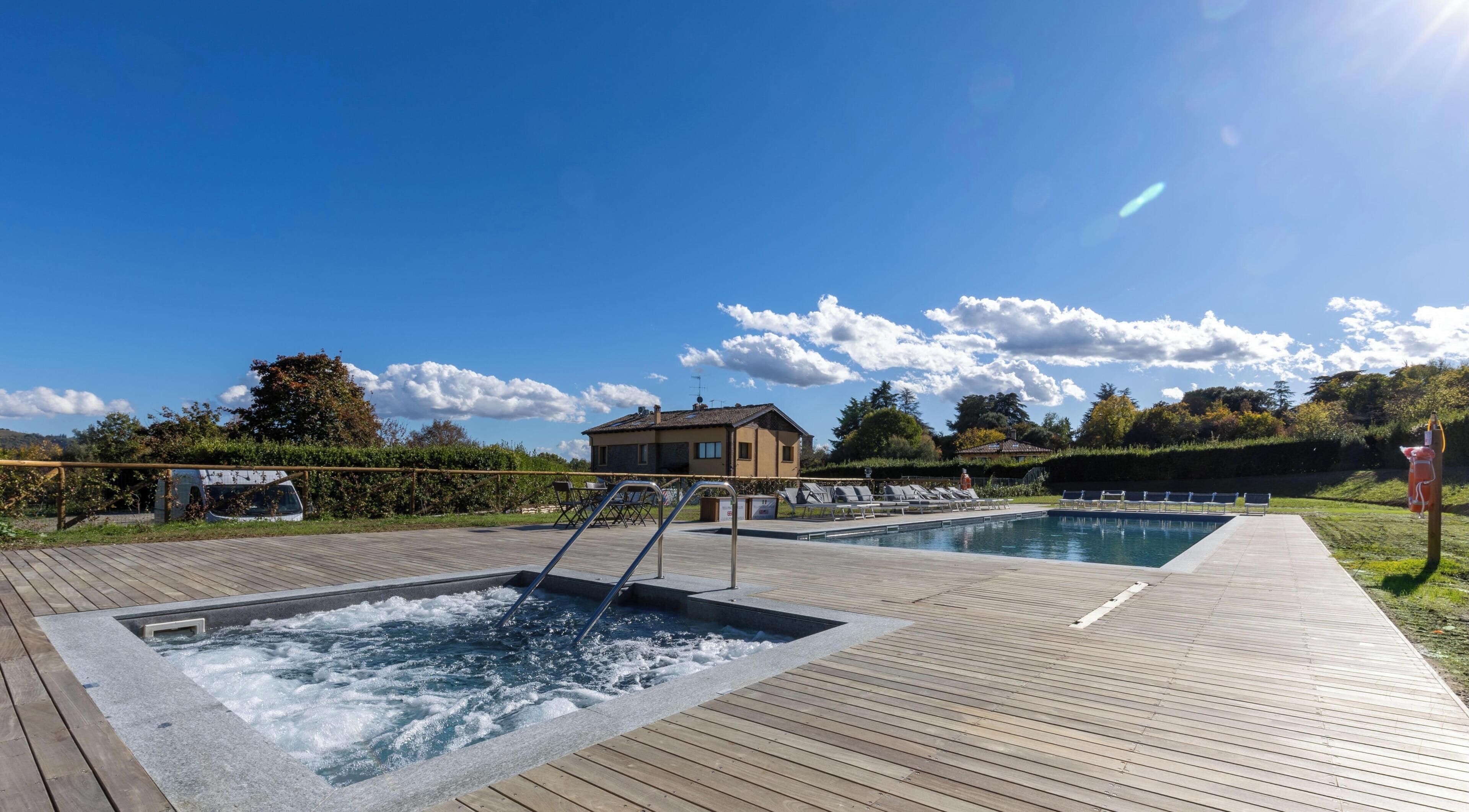 A pool area with two hot tubs and a wooden deck.