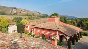 A red-roofed building with a courtyard, surrounded by greenery and hills. - Borgo Malvasia- Ca' Palazzo (Sasso Marconi)