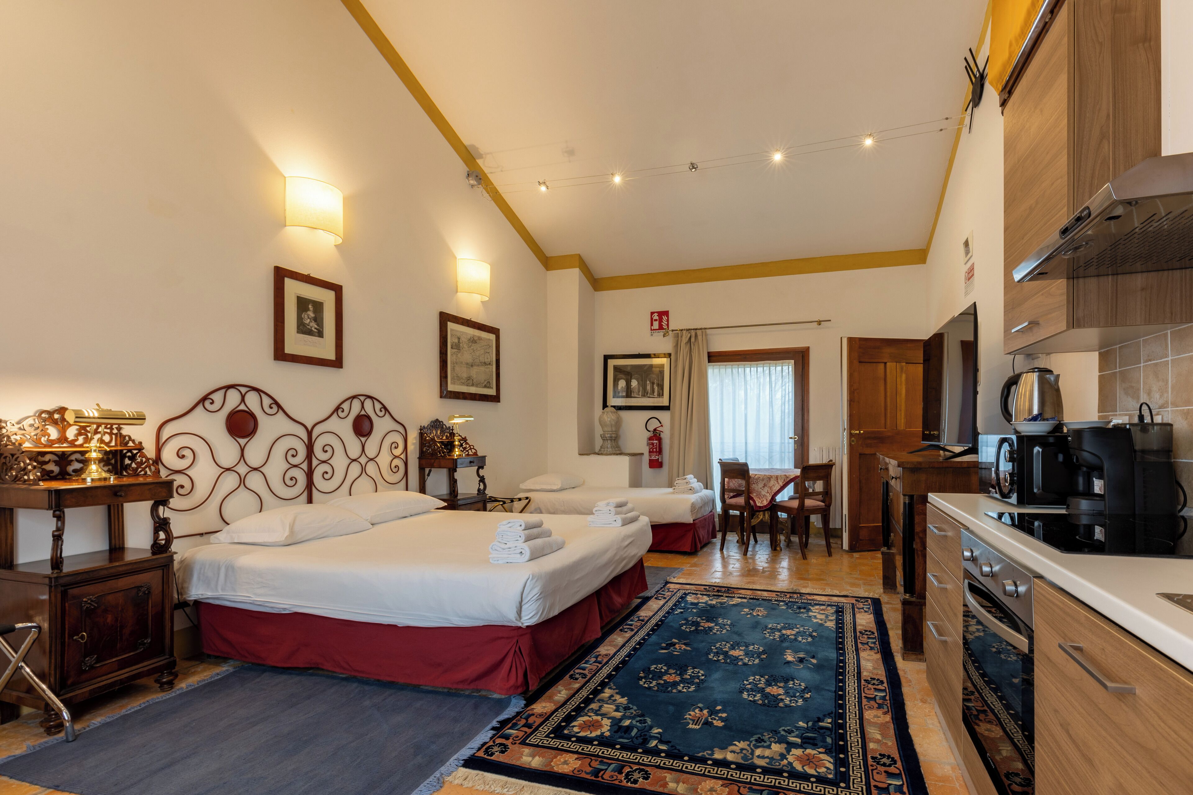 Habitación de hotel con dos camas, una zona de cocina y una mesa de comedor.