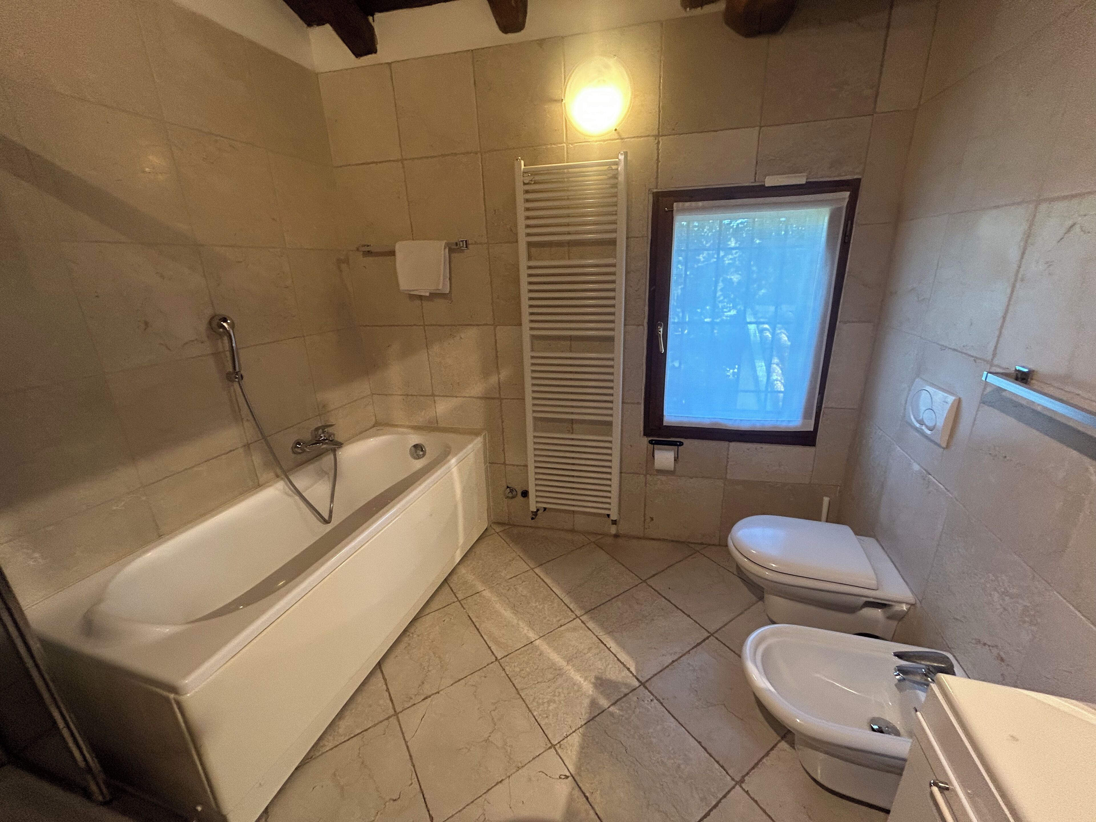 Een badkamer met een bad, toilet en een raam.