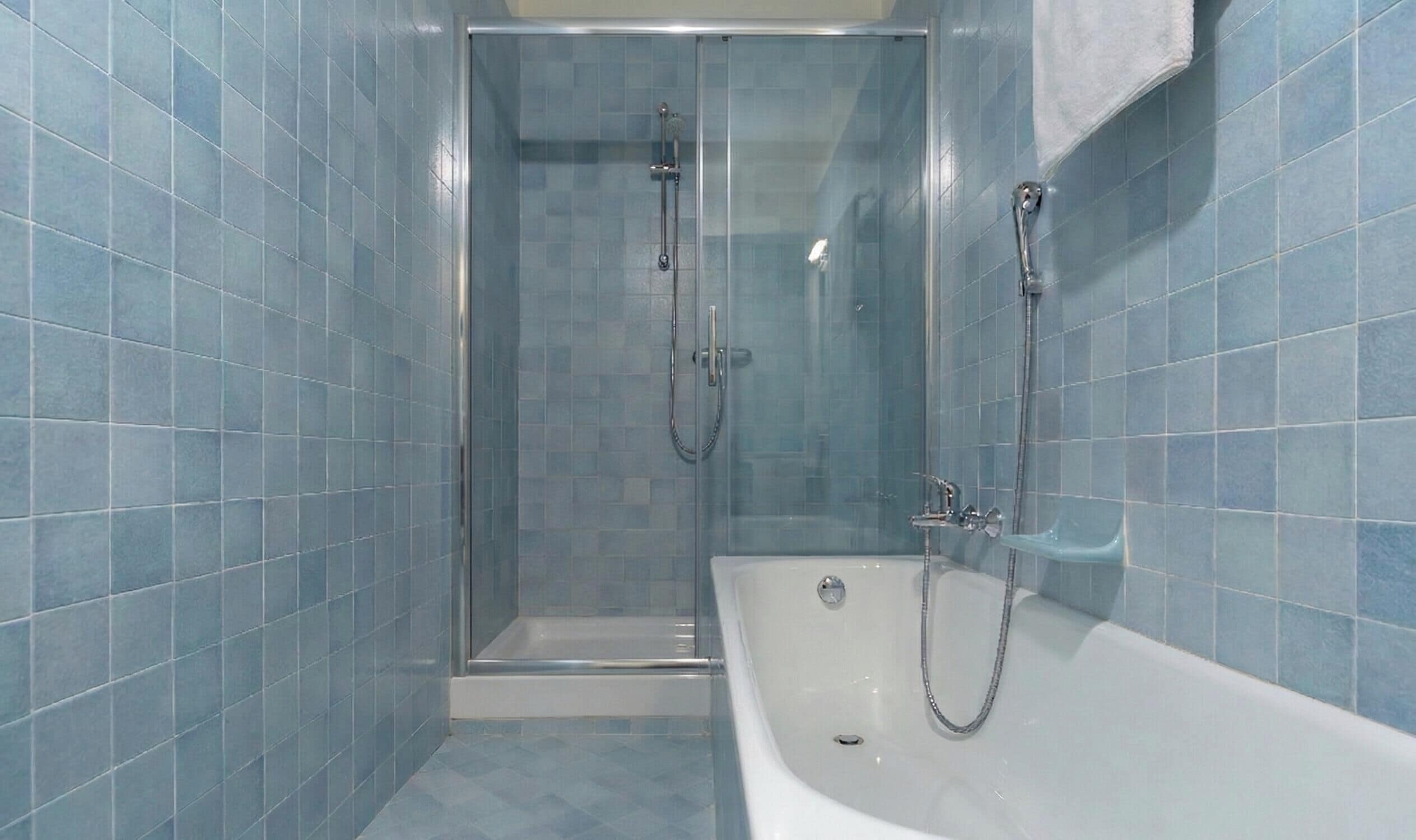 A bathroom with a glass-enclosed shower, a white bathtub, and blue-tiled walls.