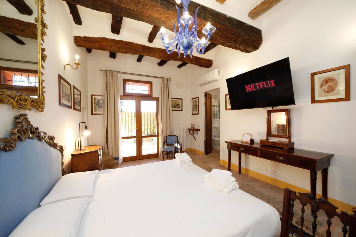 Une chambre d’hôtel avec un grand lit, un téléviseur fixé au mur, un lustre et des poutres en bois au plafond.