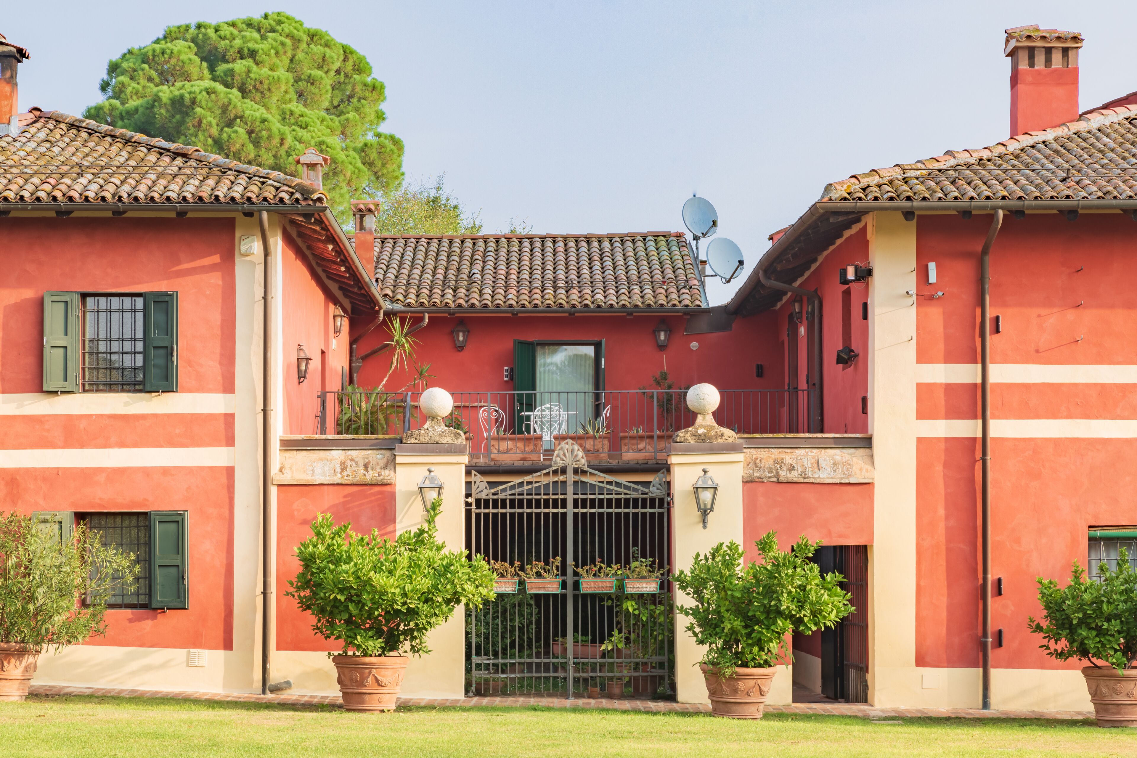 A red building with a tiled roof, a gated entrance, and satellite dishes.