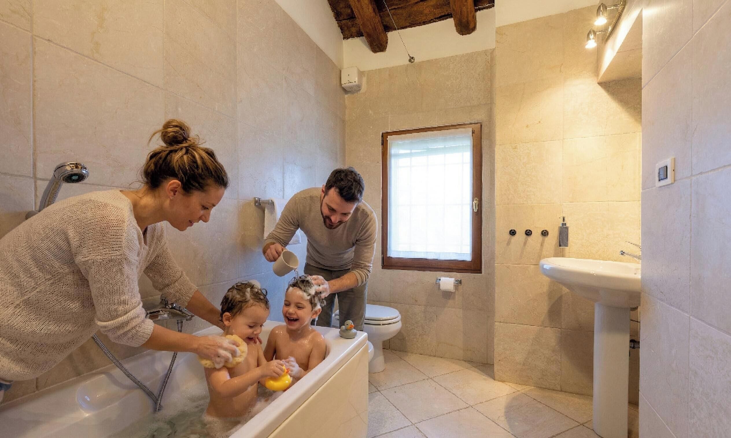 Una familia en un baño con bañera, ventana y lavamanos.