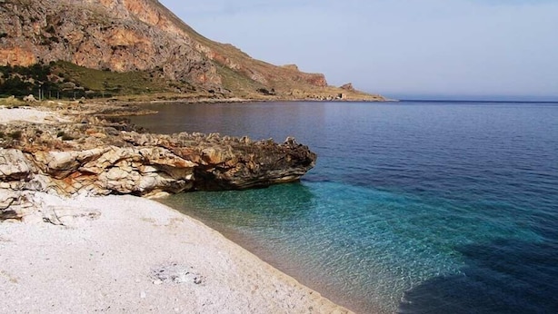 A coastal landscape with a rocky shoreline, clear blue water, and a prominent hill in the background. - B&B La Mia Isola (San Vito Lo Capo)