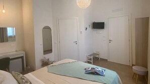 A bedroom with a bed, bedside tables, a desk, a chair, a TV, and a hanging light fixture. - B&B La Mia Isola (San Vito Lo Capo)