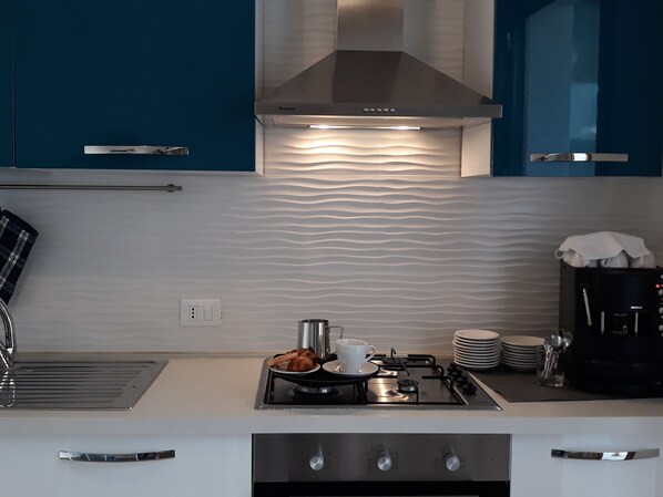 Una cocina moderna con estufa a gas, cafetera y pileta.