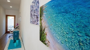 A hallway with a large mural of a beach scene, a reception desk, and a chair. - B&B La Mia Isola (San Vito Lo Capo)
