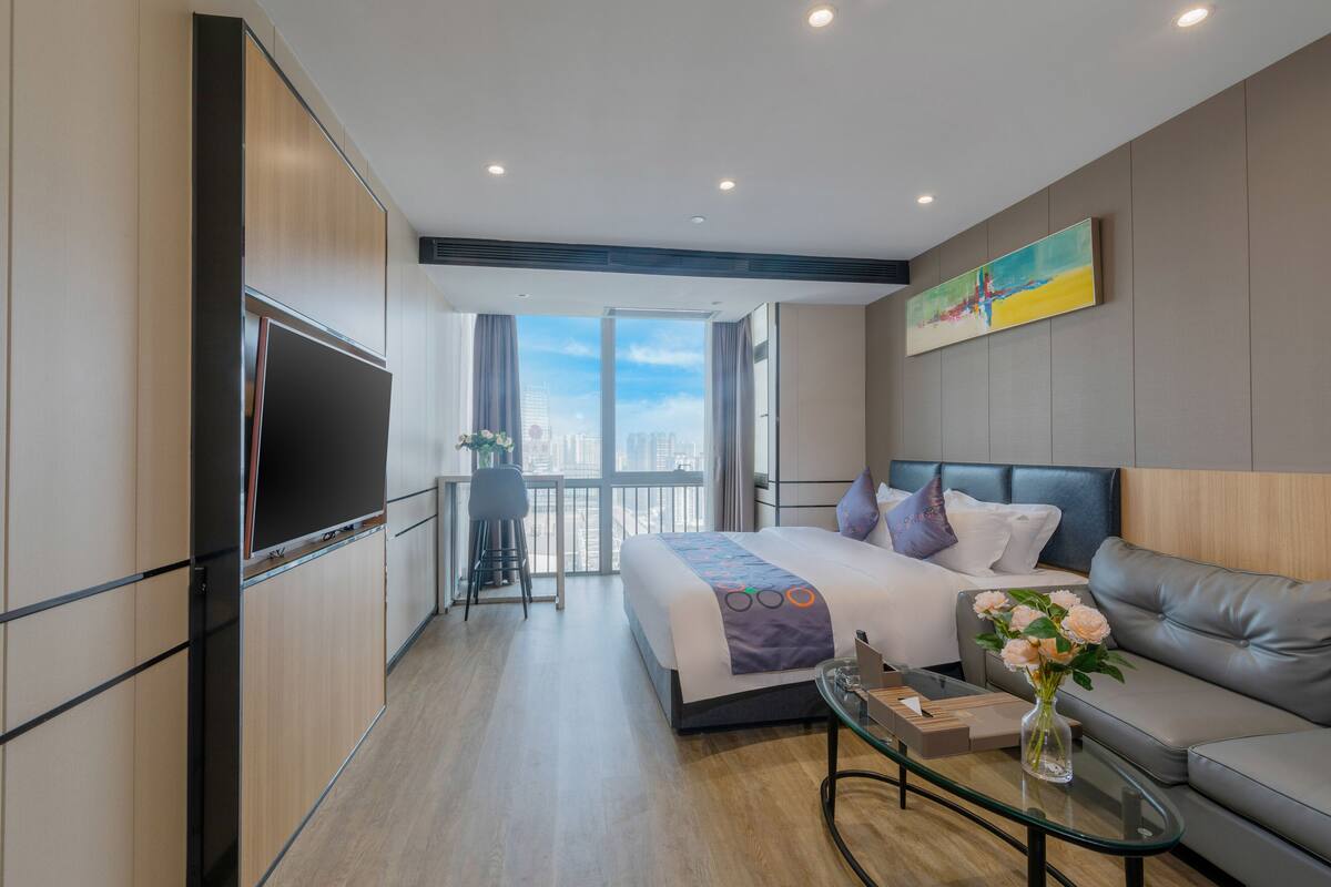 A modern hotel room with a large bed, a sofa, a glass coffee table, and a TV.