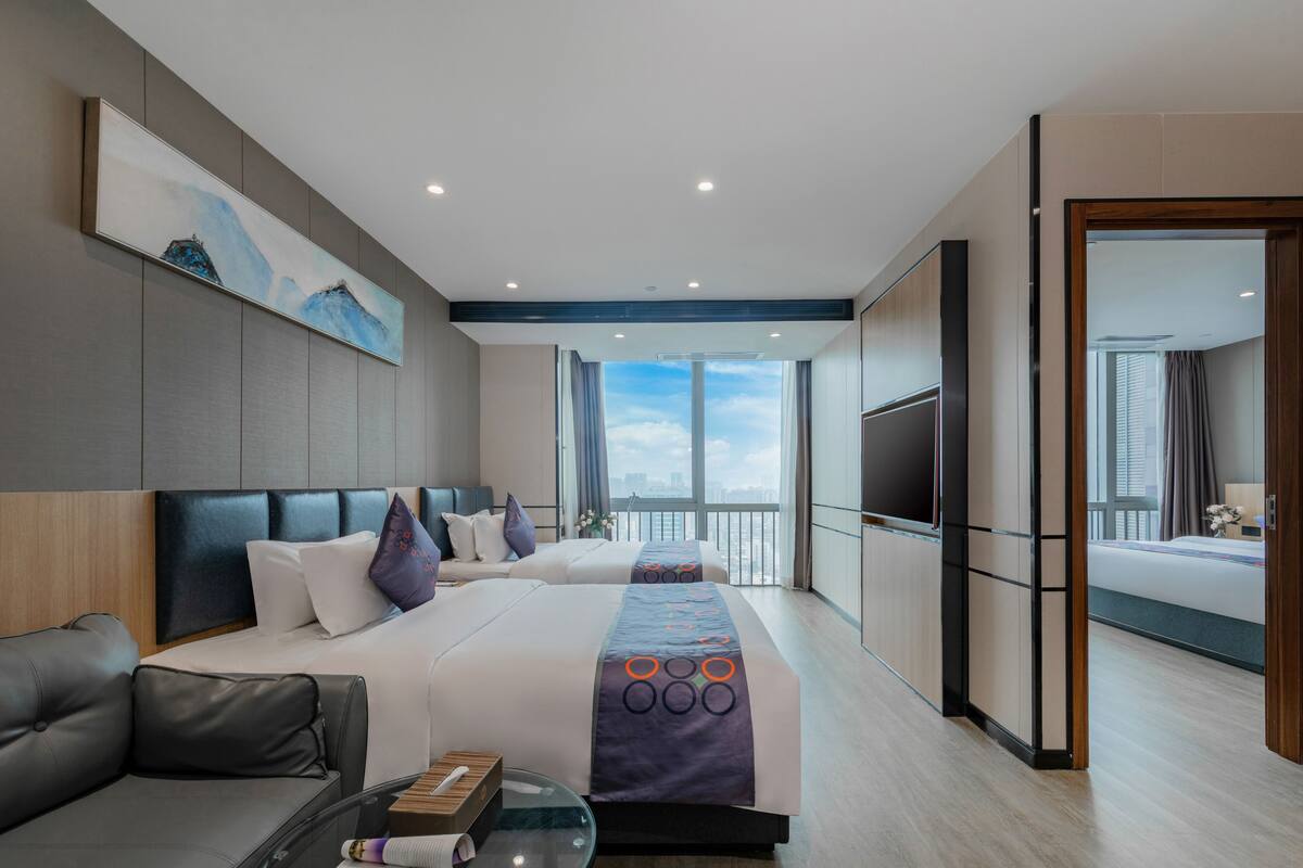 A modern hotel room with a large bed, a sofa, a TV, and a balcony with a city view.