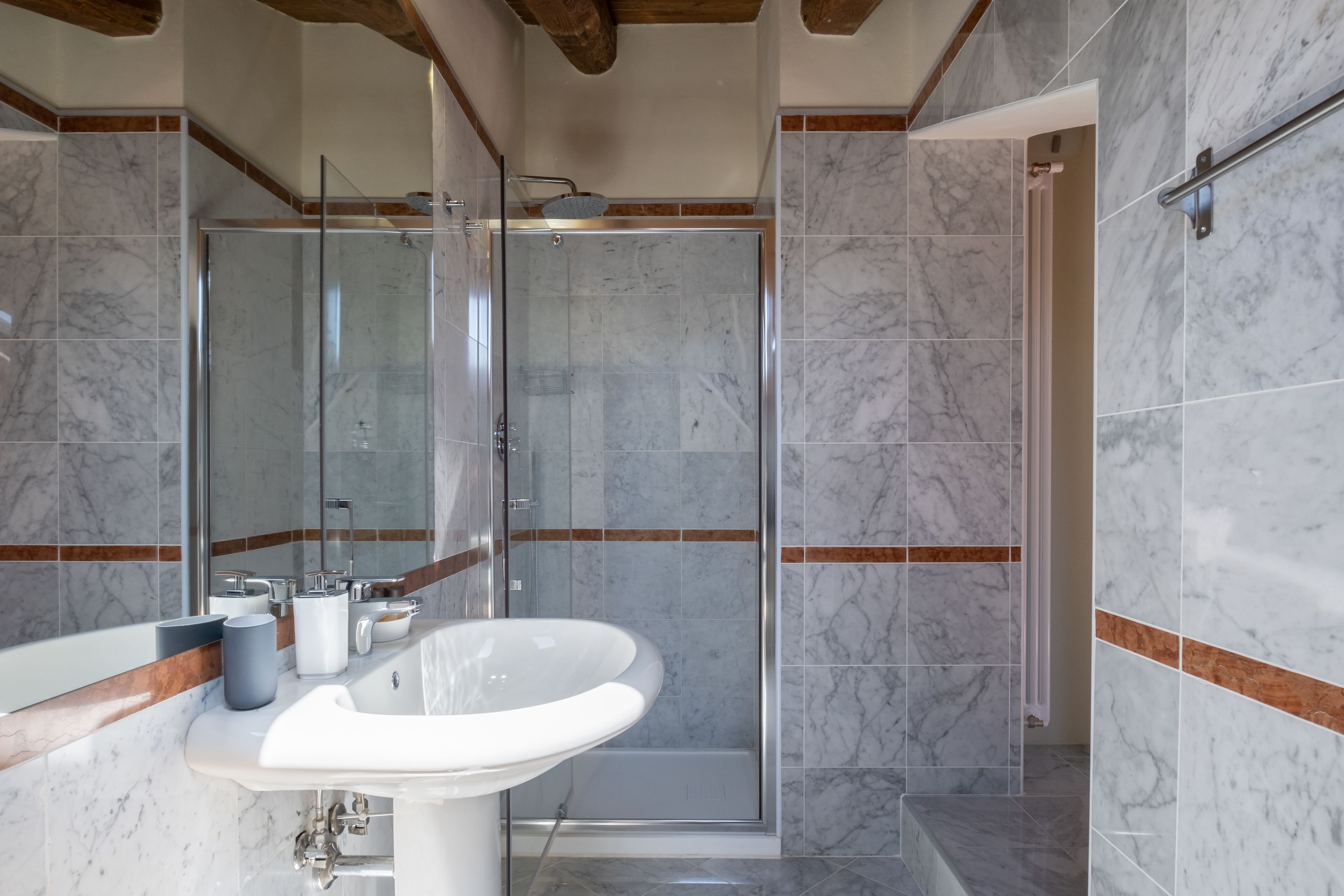 A modern bathroom with a glass shower enclosure, a white sink, and marble tiles.