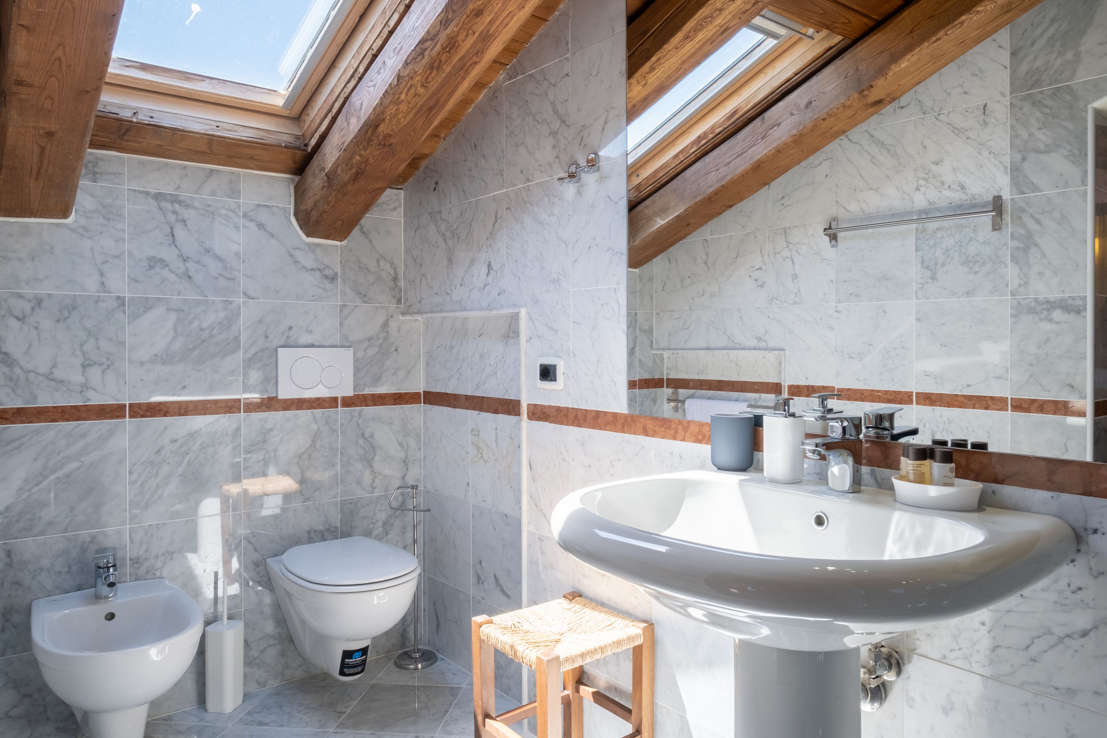 Ein Badezimmer mit Dachfenster, Marmorfliesen, einem Waschbecken, einer Toilette und einem Bidet.