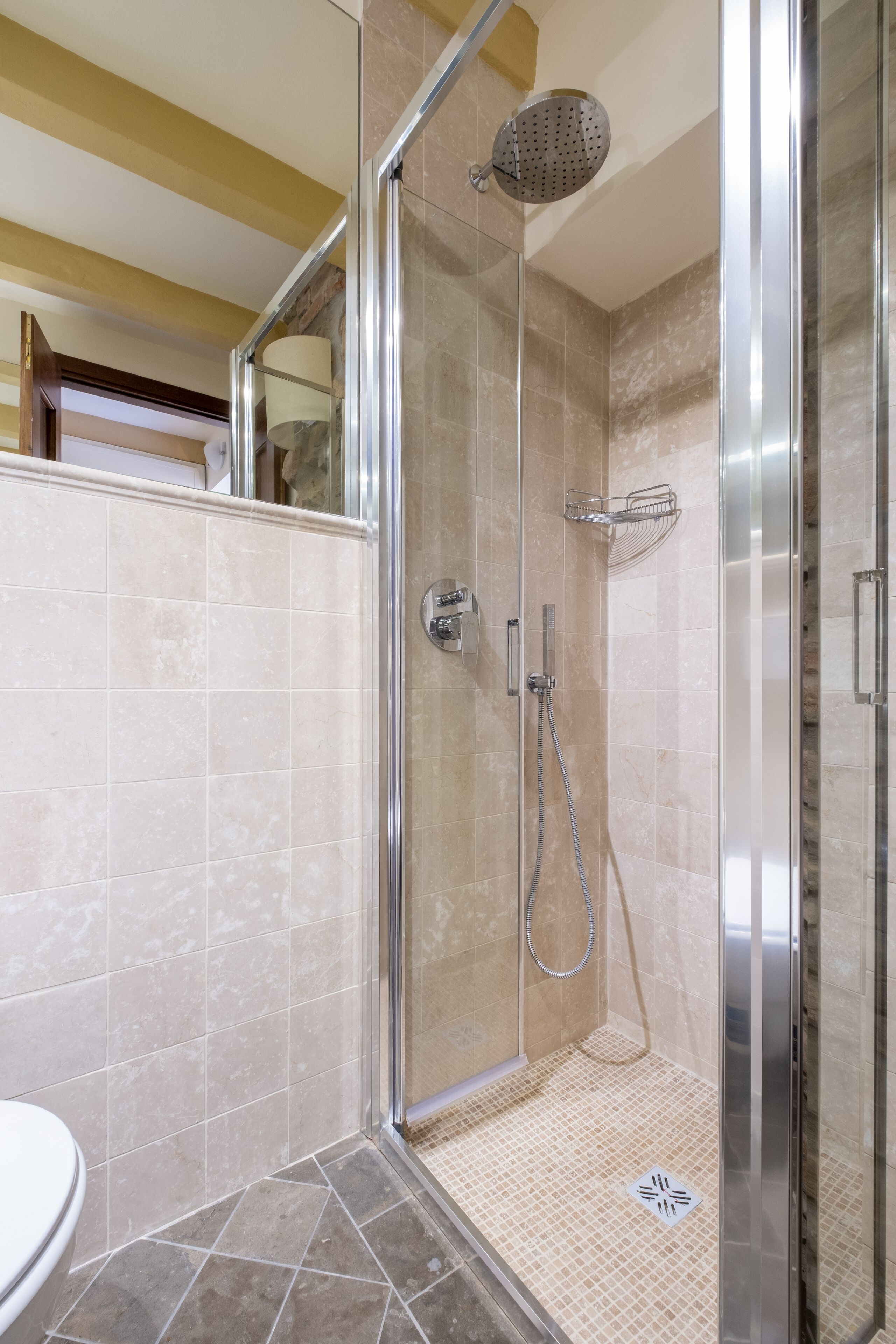 A modern bathroom with a glass-enclosed shower, beige tiles, and a visible toilet.