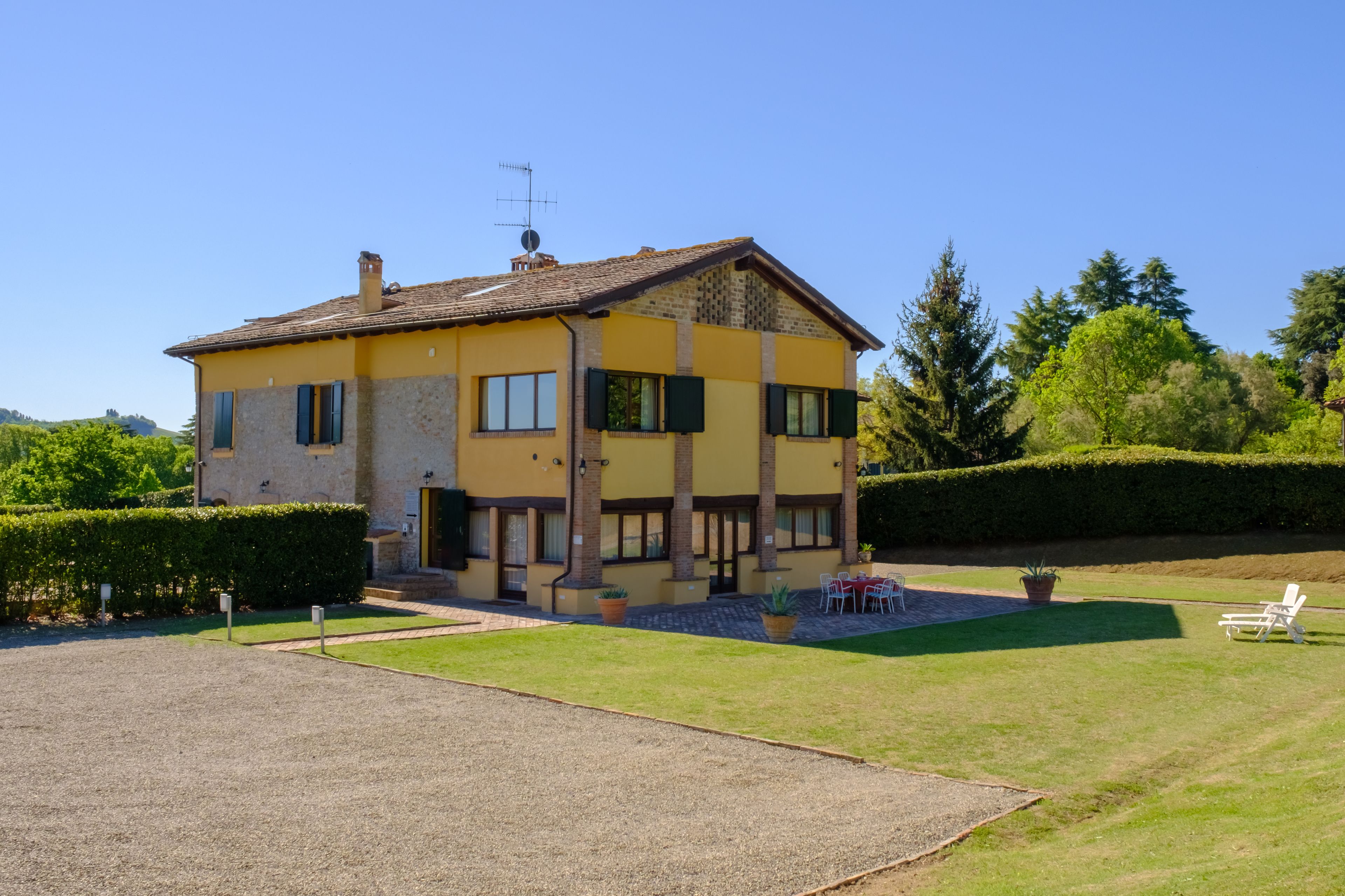 A two-story house with a yellow facade, a gravel driveway, and a well-maintained lawn.