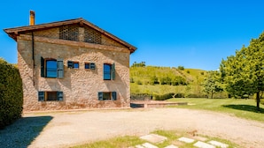 Un edificio de piedra con techo inclinado, varias ventanas y un camino de grava que conduce a una zona con césped.