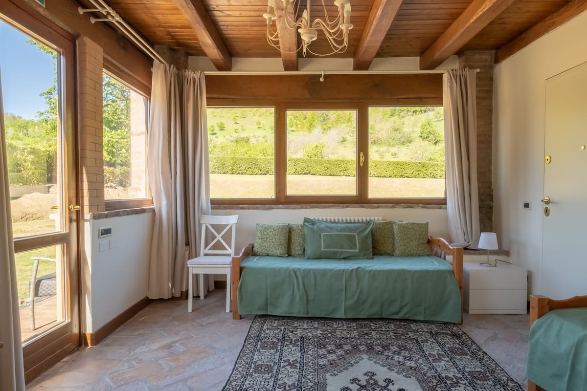 Ein gemütliches Zimmer mit einem grünen Bett, einem gemusterten Teppich und Blick ins Grüne.