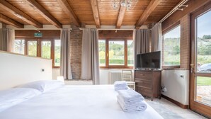 Habitación de hotel con una cama grande, televisión, cómoda y vistas al exterior a través de amplias ventanas.