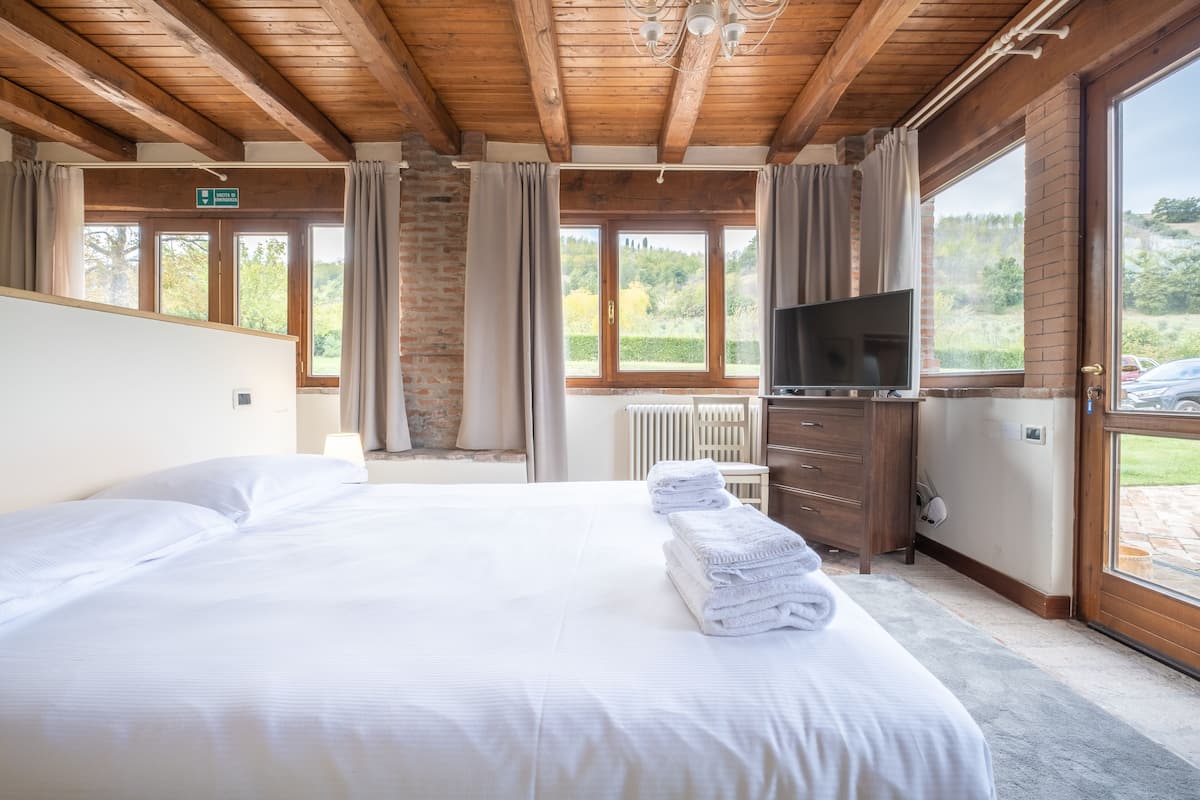 Ein Hotelzimmer mit einem großen Bett, einem Fernseher, einem Schminktisch und Blick ins Freie durch große Fenster.