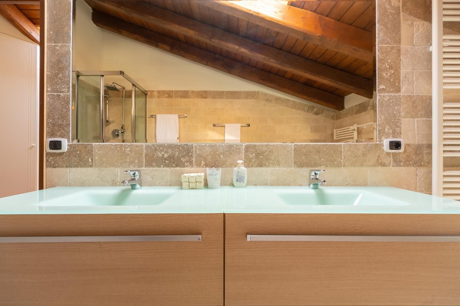 Een badkamer met twee wastafels, houten kastjes, een spiegel en een betegelde wand.