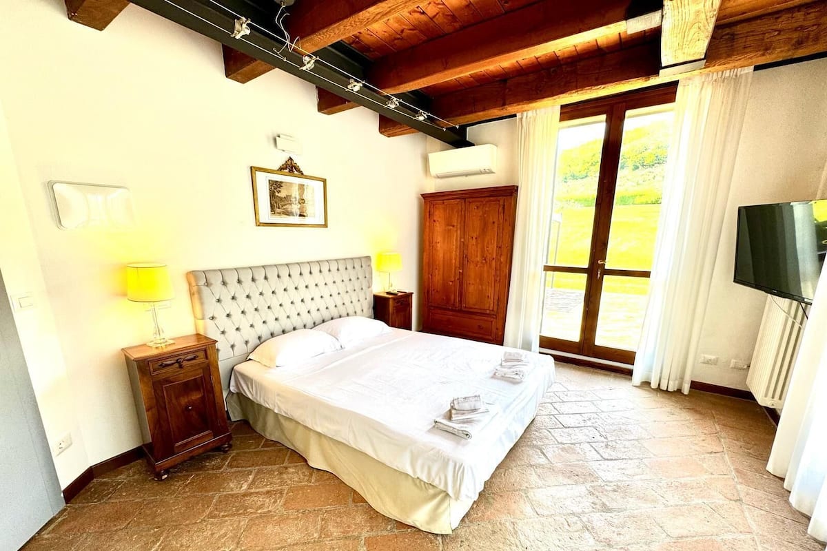 Ein Schlafzimmer mit einem großen Bett, einem Holzschrank, einem Fernseher und einem Fenster mit Vorhängen.