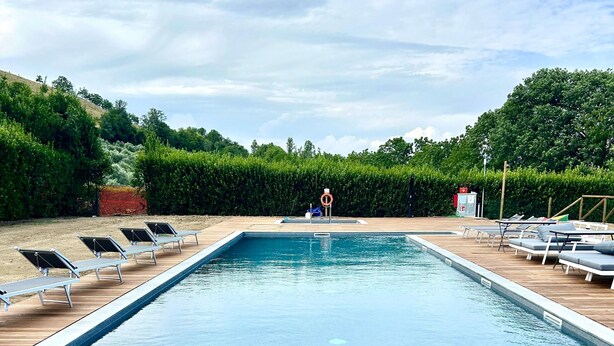 Una piscina rectangular con muelle de madera y sillas de descanso.