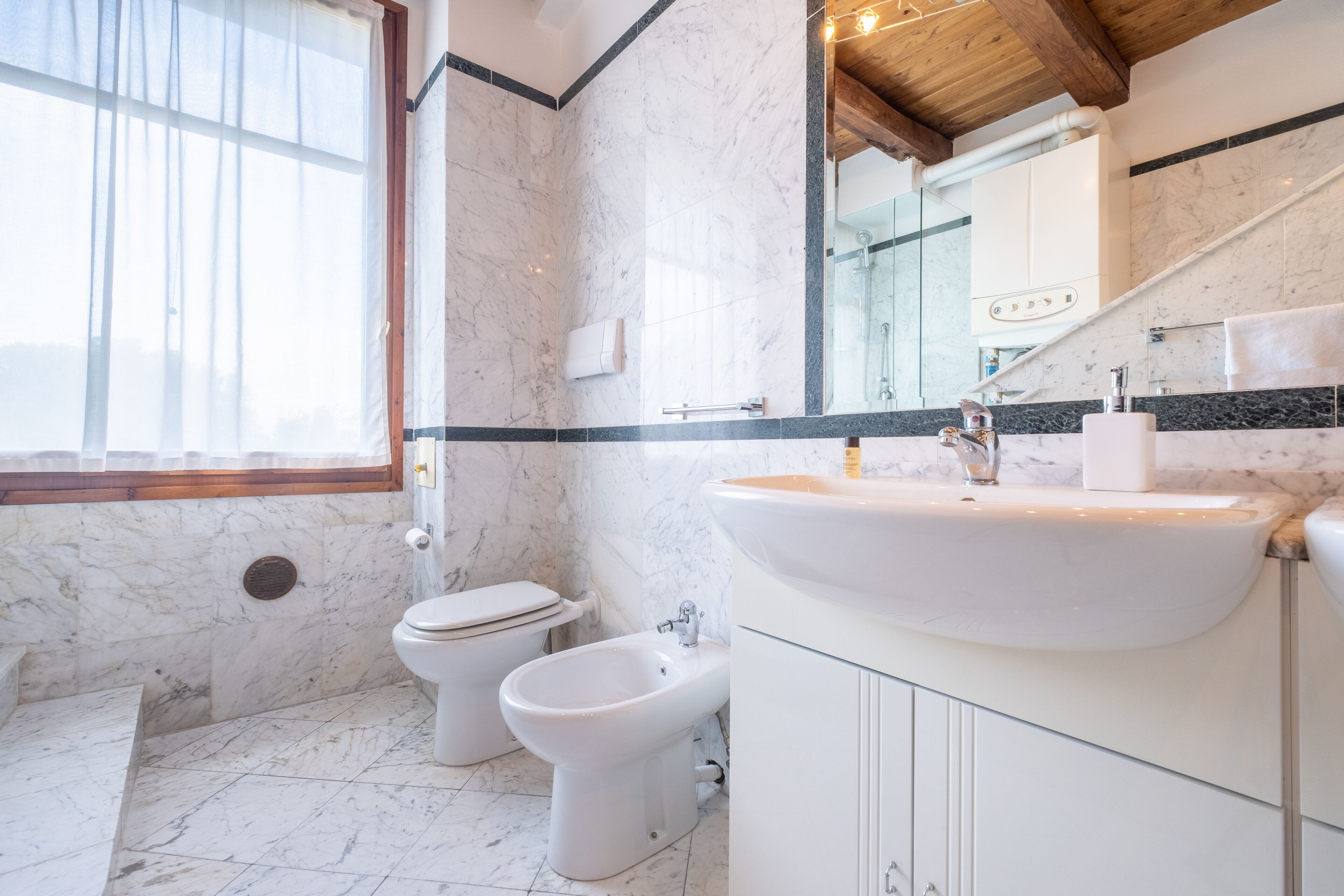 A bathroom with a marble floor, a white sink, a bidet, and a toilet.