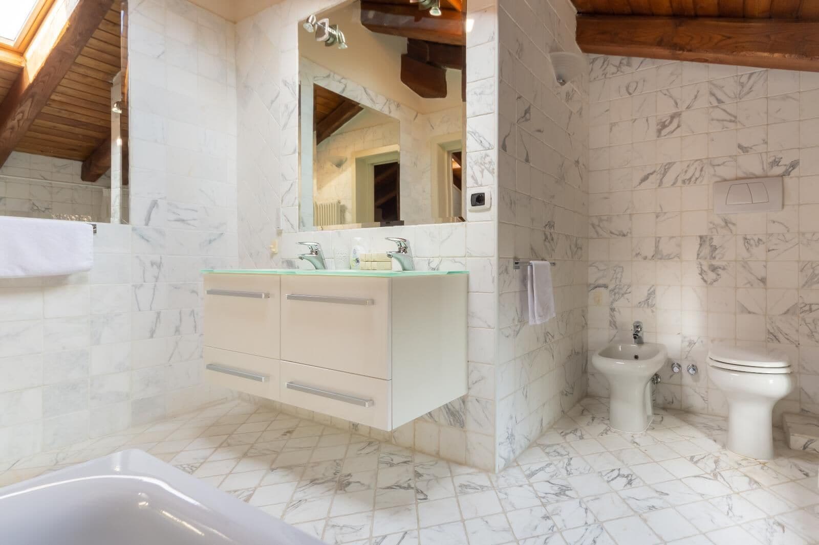 Een badkamer met een marmeren vloer, een vrijstaand bad, een wastafel met spiegel en een toilet.