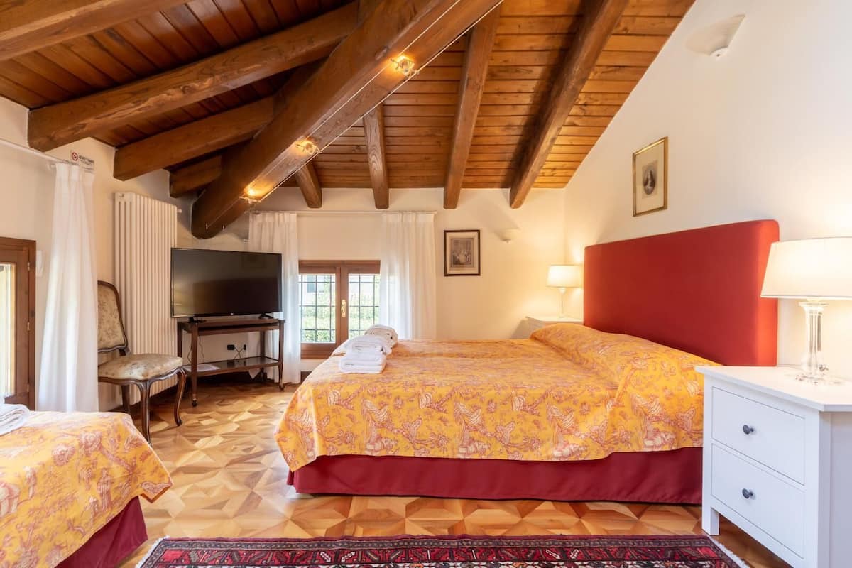 Ein Schlafzimmer mit Holzboden, einem Bett mit rotem Kopfteil, einem Fernseher und einem Fenster mit Vorhängen.
