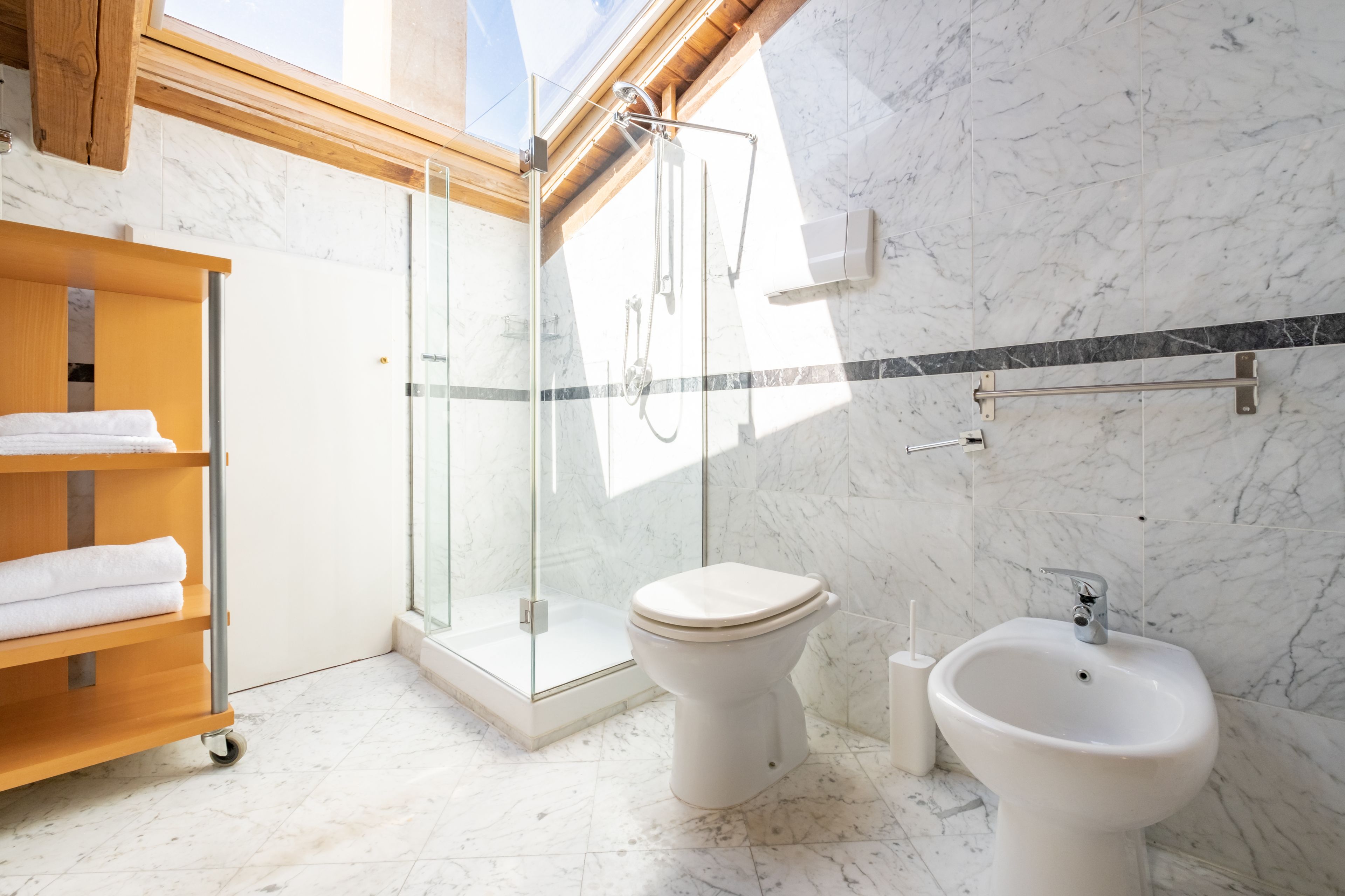 Un baño moderno con ducha envuelta en vidrio, inodoro, bidé y estante de madera con toallas.