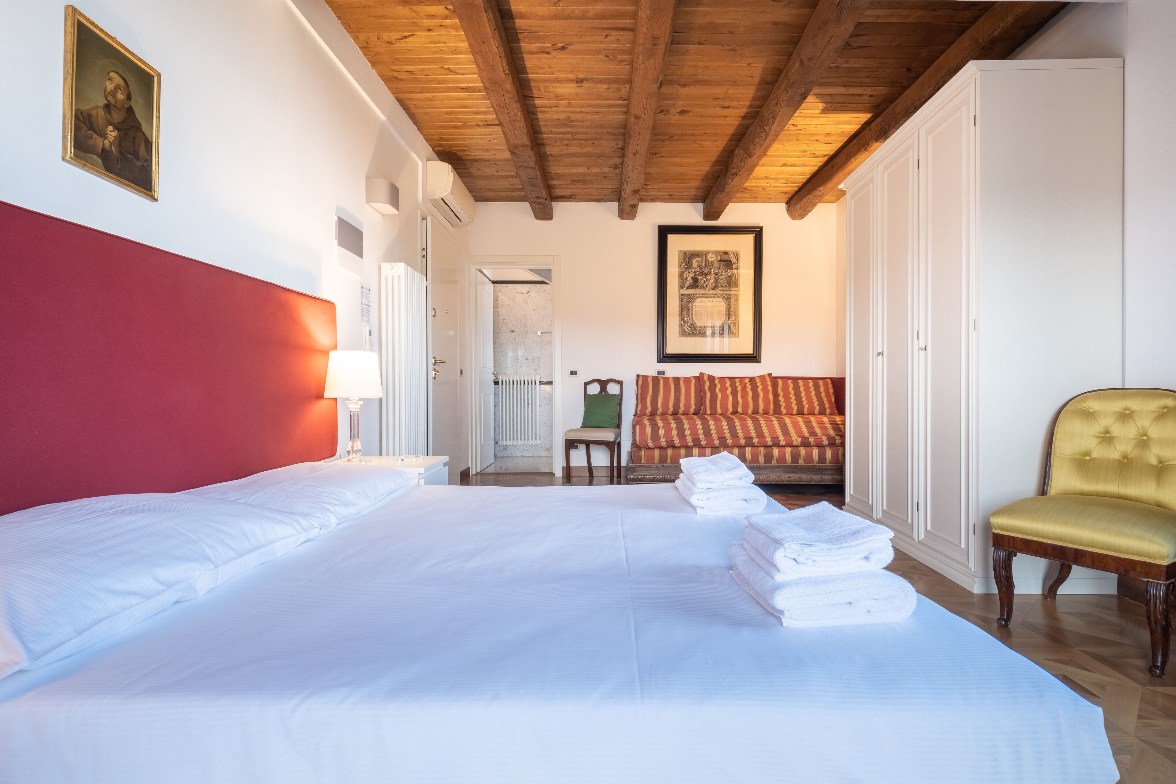 Ein Hotelzimmer mit einem großen Bett, einem roten Kopfteil, einem gelben Sessel und einem gerahmten Bild an der Wand.