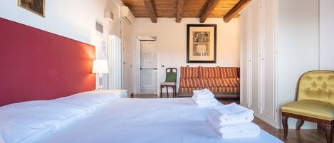 Quarto de hotel com uma cama grande, cabeceira vermelha, poltrona amarela e um quadro na parede.