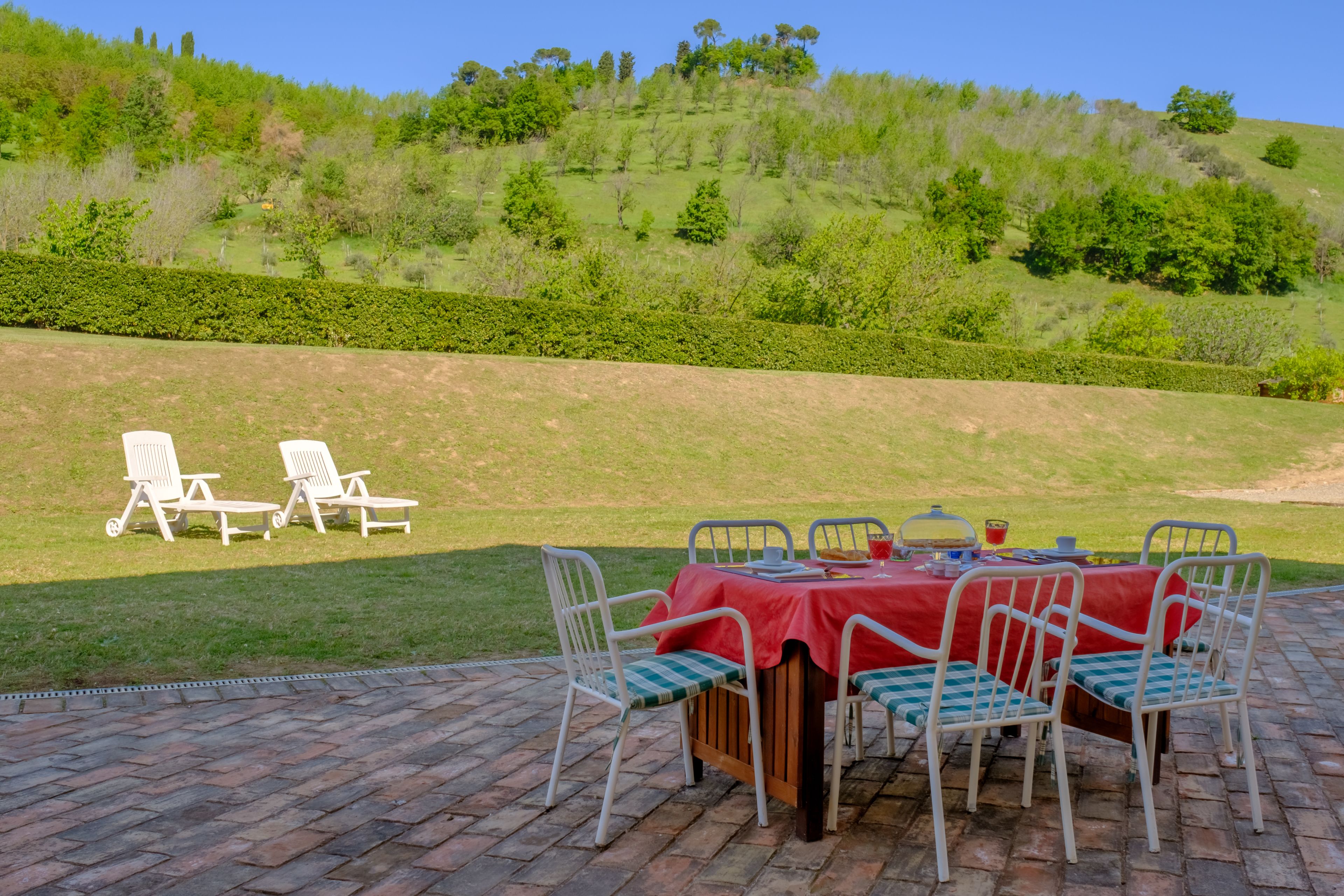An outdoor dining area with a brick patio, a table with a red tablecloth, and chairs with checkered cushions.
