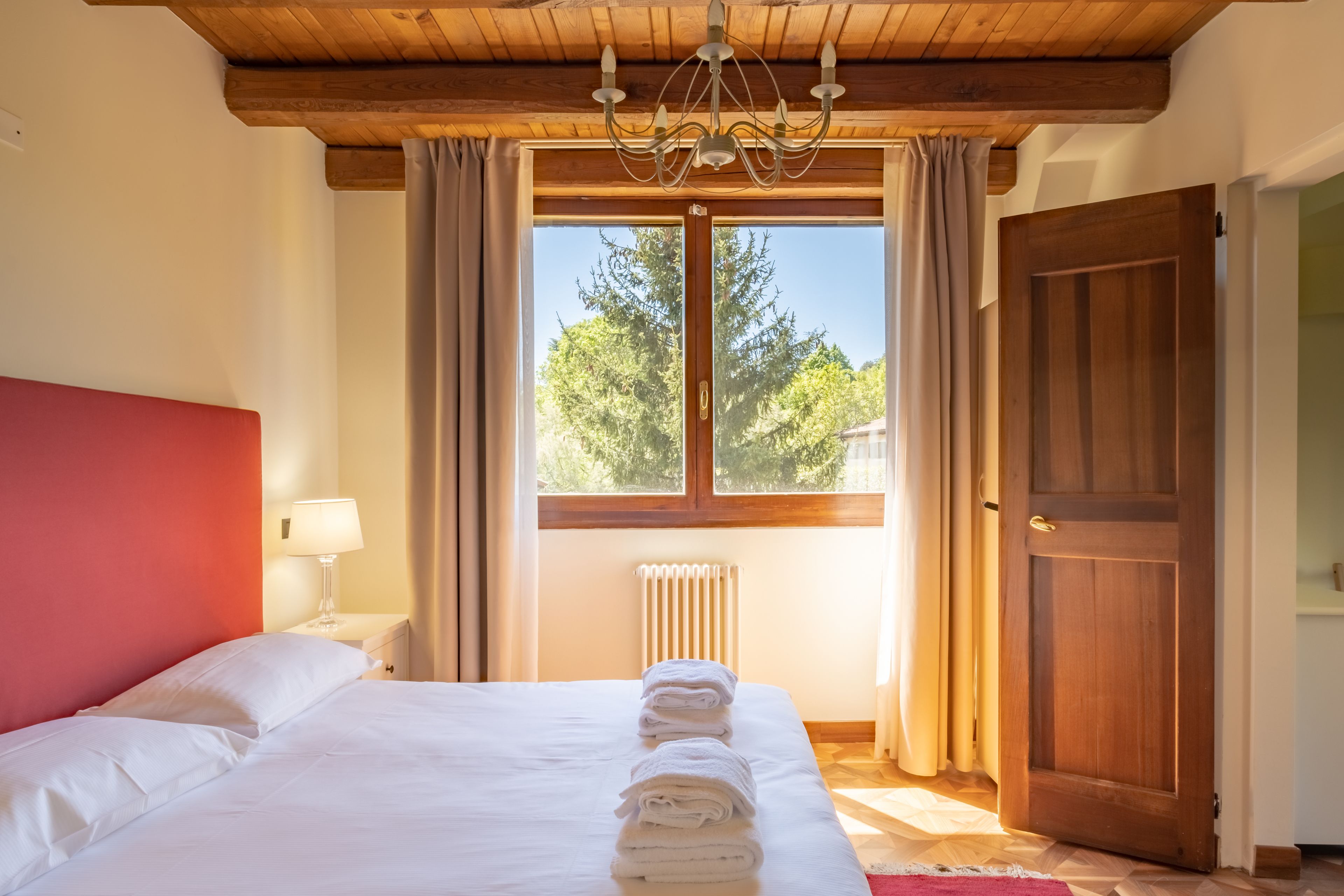 Une chambre d’hôtel avec un grand lit, un plafond en bois, une fenêtre avec des rideaux et une porte.