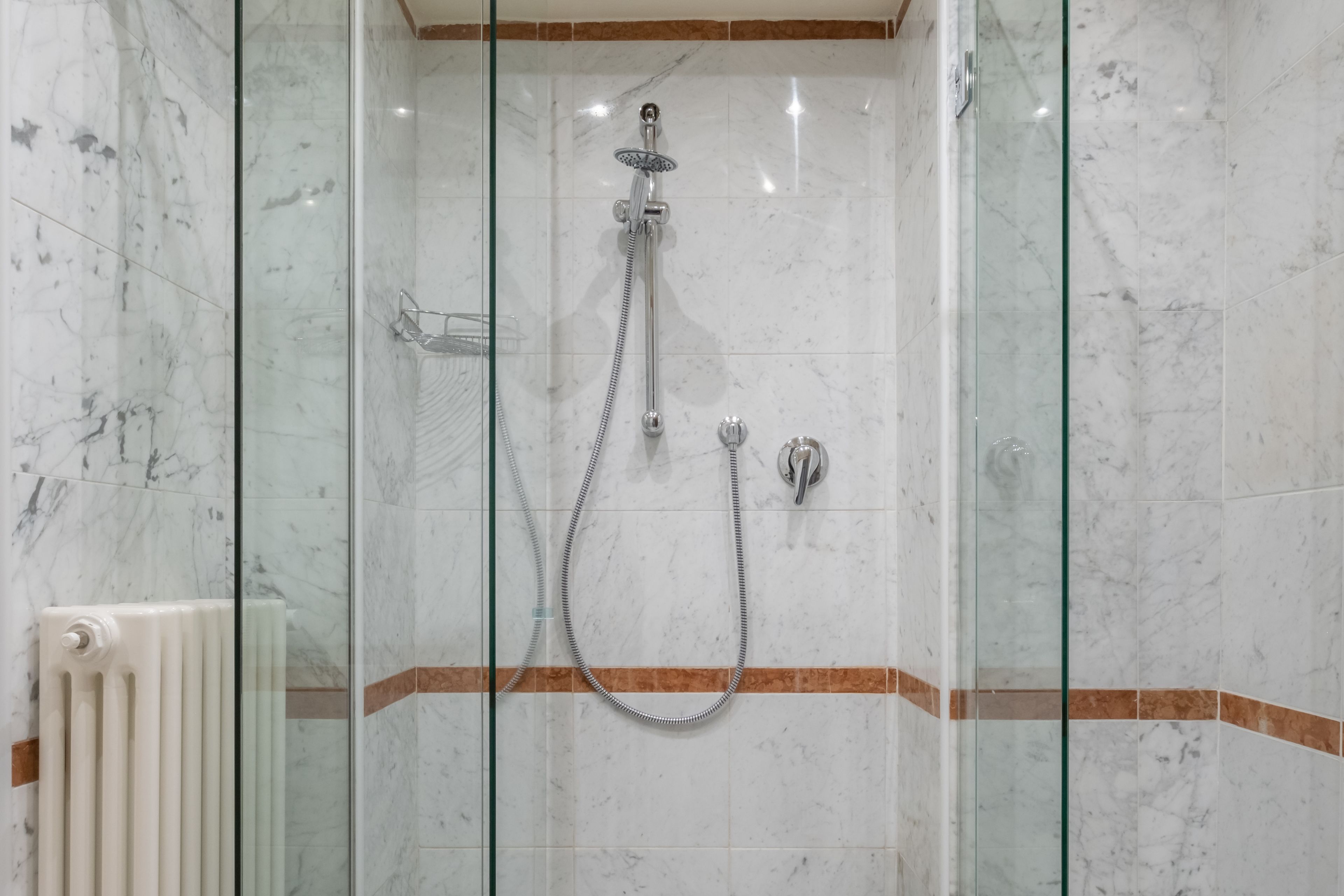 A glass-enclosed shower with a handheld showerhead and a fixed wall-mounted faucet.